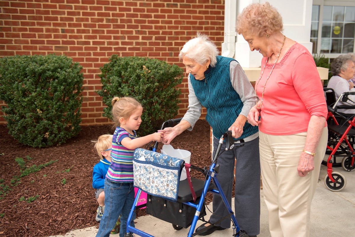 A heartwarming interaction between children and elderly women outdoors near a brick wall.