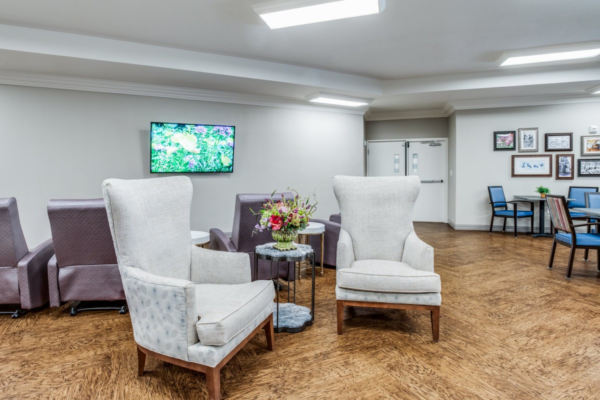 A modern living room with armchairs, a small table with flowers, and a wall-mounted television.