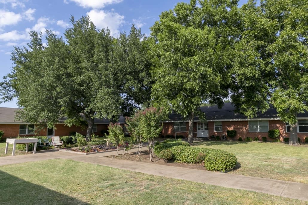 A brick house surrounded by trees and a well-maintained lawn.