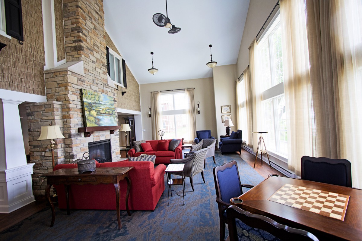 A modern living room featuring large windows, a stone fireplace, and comfortable seating with red and blue sofas.