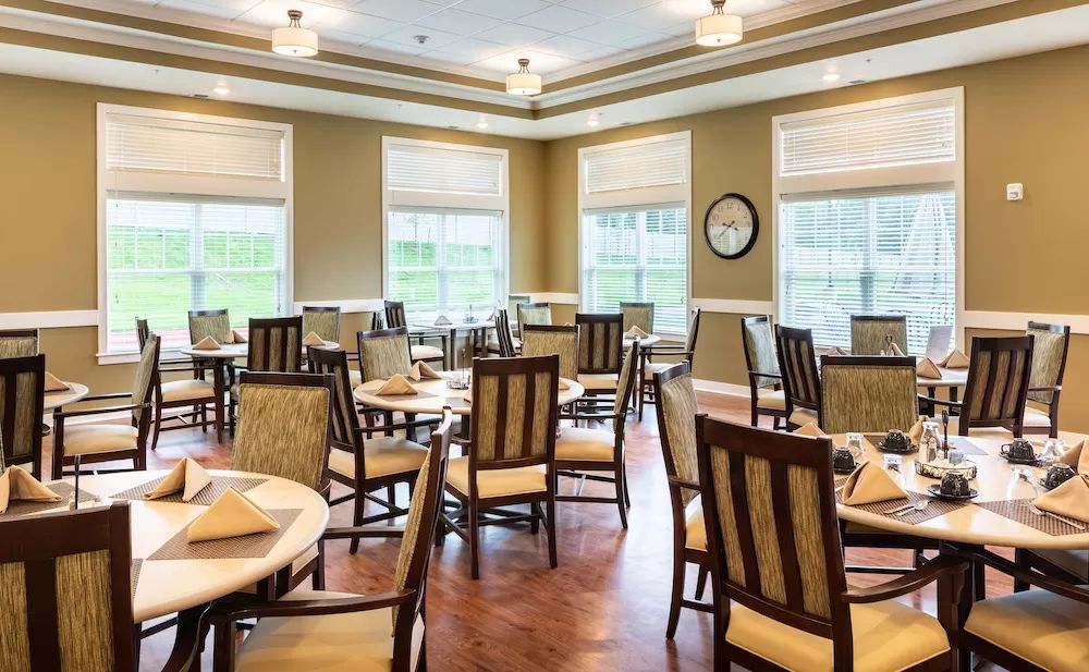 A well-lit dining room with multiple tables and chairs, featuring large windows and modern decor.