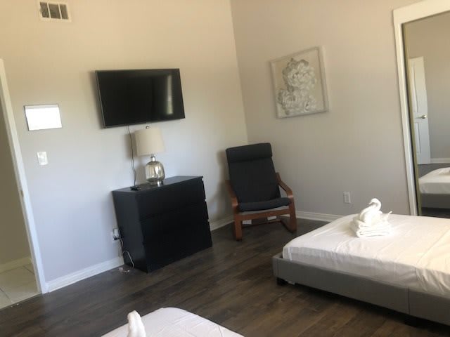 A minimalist bedroom featuring a mounted television, a chair, and a small table lamp.