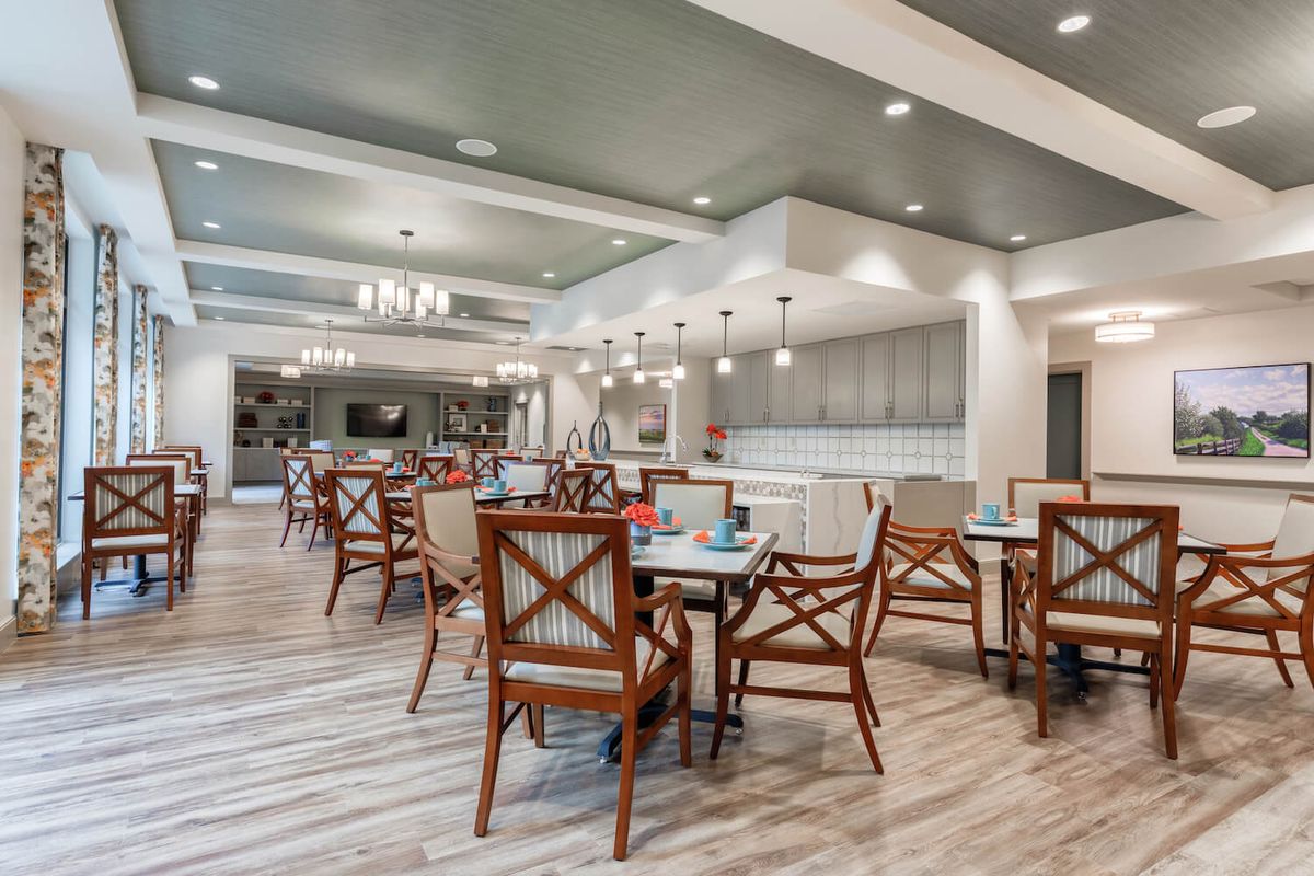A stylish and modern dining area with neatly arranged tables and chairs, illuminated by elegant chandeliers.