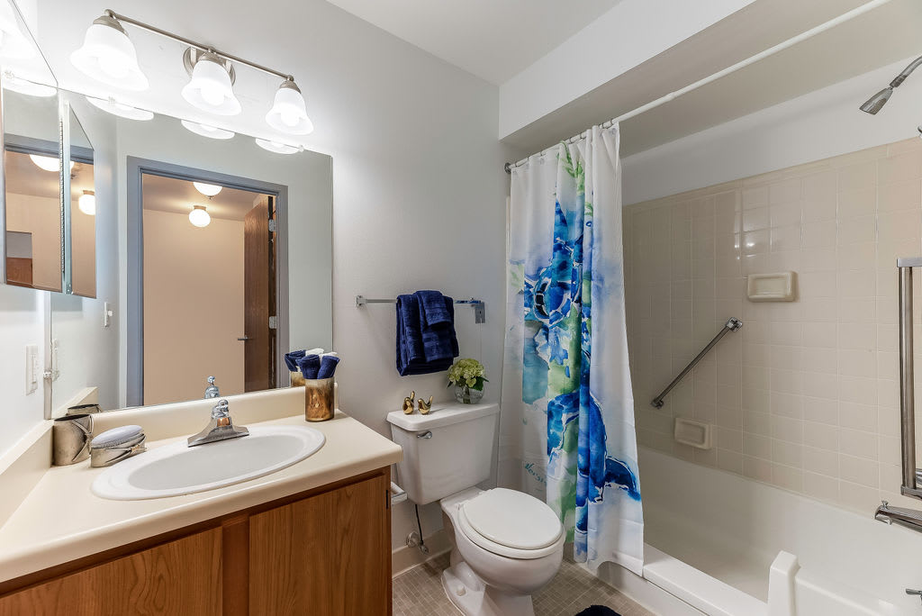 A clean and modern bathroom with a sink, mirror, toilet, and shower with a colorful curtain.