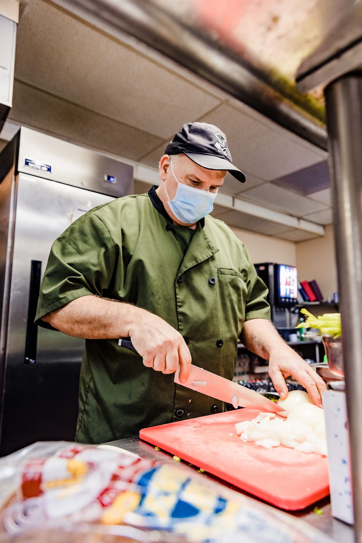 A chef is chopping ingredients on a red cutting board in a professional kitchen.