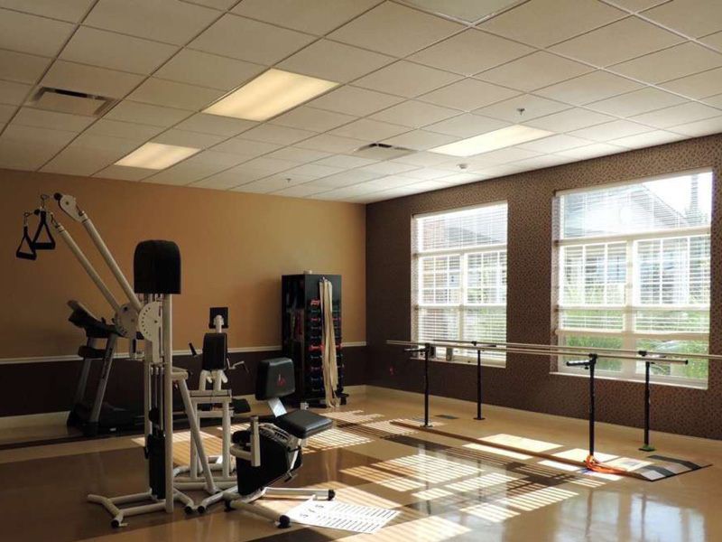 A well-lit gym with various fitness equipment and large windows.