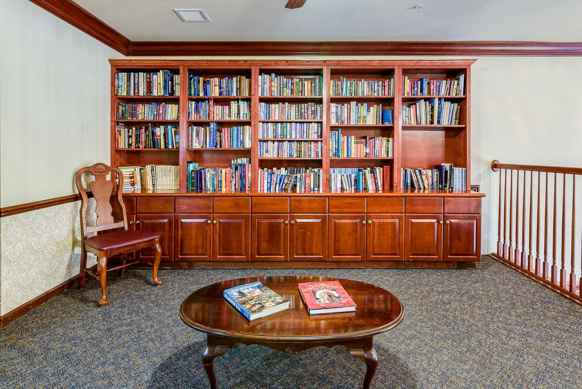 A cozy library room with a large wooden bookshelf filled with books and a table displaying two open books.