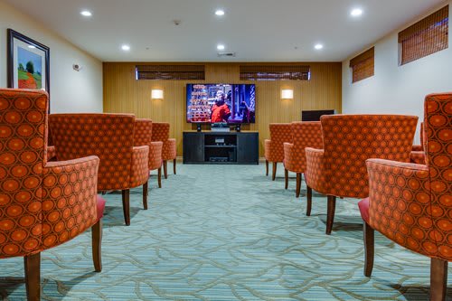 A small theater room with rows of upholstered chairs facing a large television screen.
