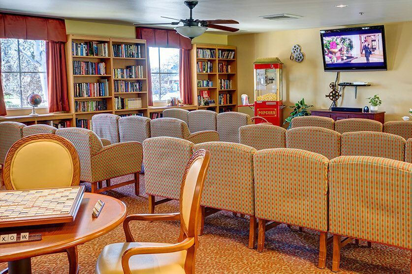 A cozy reading room with chairs arranged in rows, surrounded by bookshelves and featuring a television and a popcorn machine.