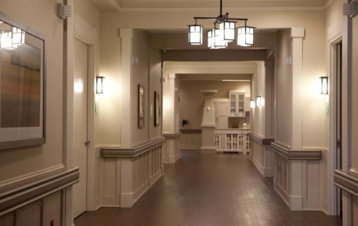 A well-lit hallway with wooden floors and neutral-toned walls leading to a distant room.