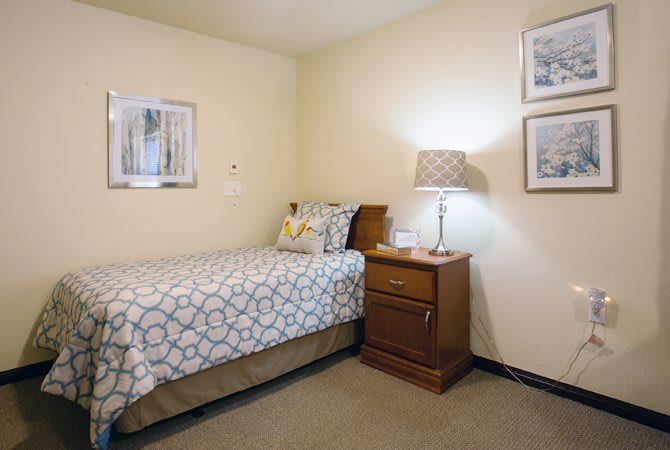 A cozy, minimalist bedroom with a single bed and nightstand under soft lighting.
