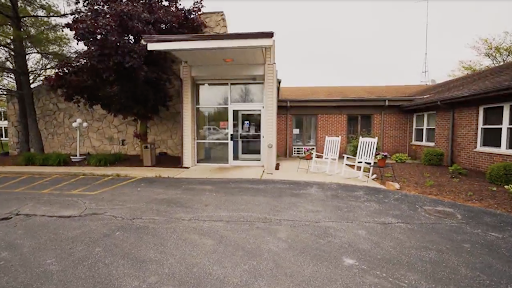 A welcoming entrance to a building with rocking chairs on the porch and landscaped surroundings.