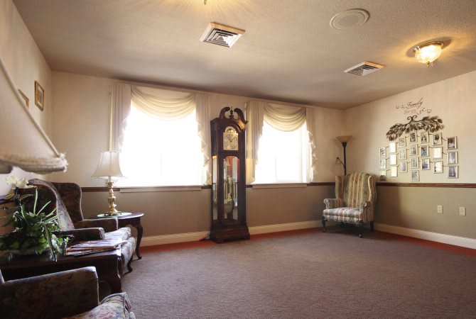 A cozy living room with a grandfather clock and armchairs by the window.