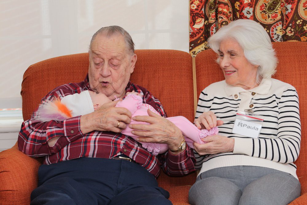 Elderly couple sitting on a couch, joyfully holding a newborn baby.