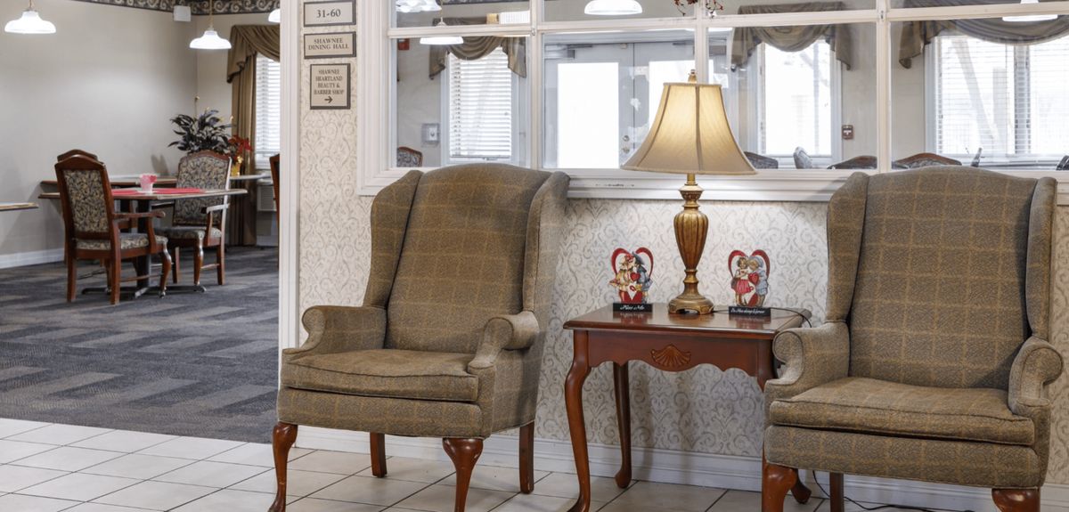 A cozy living room corner featuring a cushioned armchair, a wooden side table with a lamp, and decorative items.