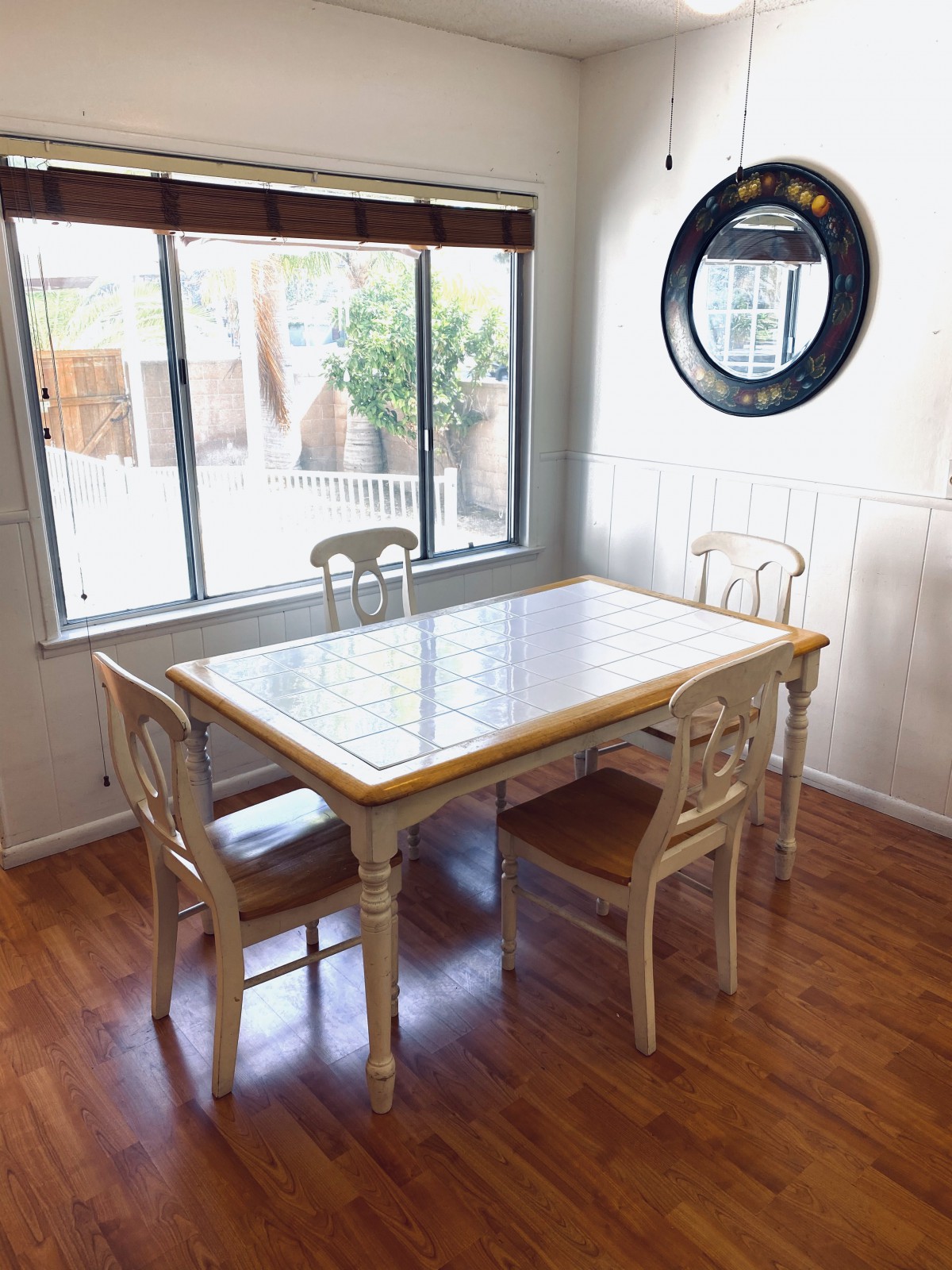 A cozy dining area with a table and four chairs, next to a large window and a decorative mirror on the wall.