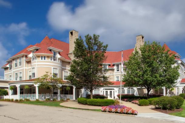A large, elegant house with a red roof and well-maintained garden under a partly cloudy sky.