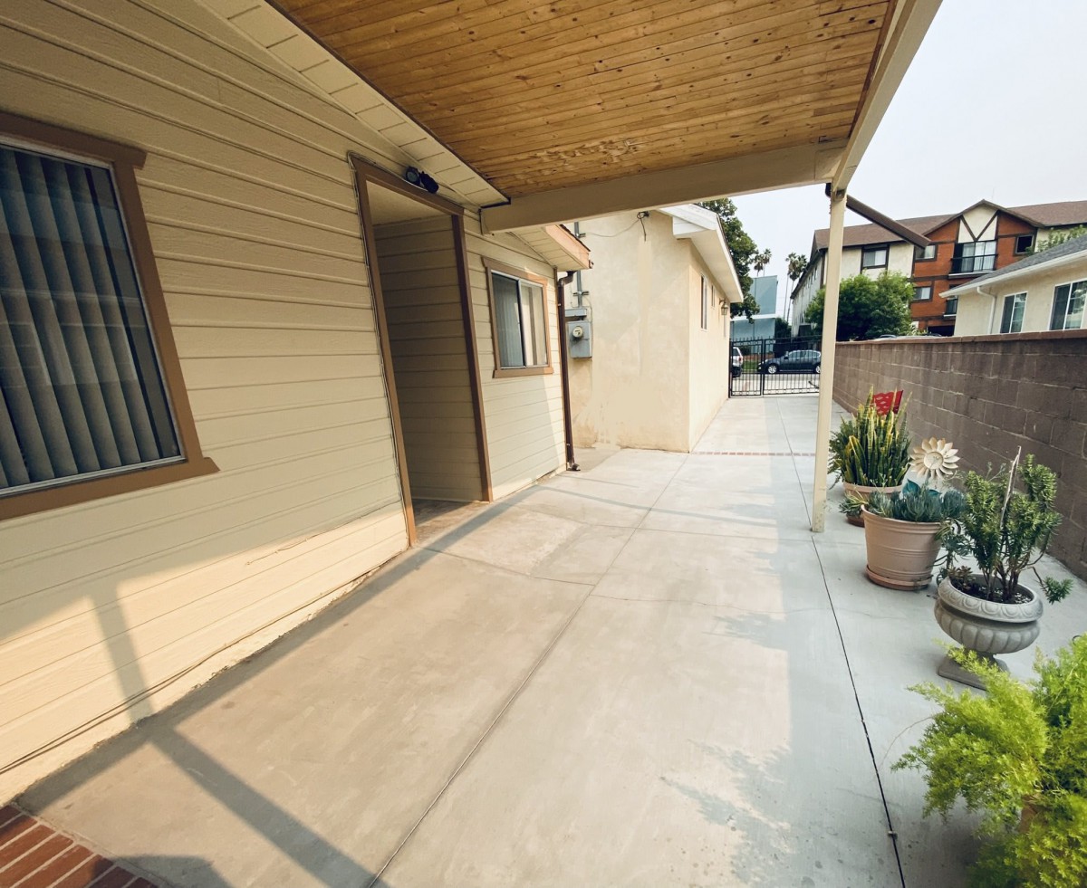 A covered patio with a concrete floor and potted plants, providing an inviting outdoor space at a residential property.