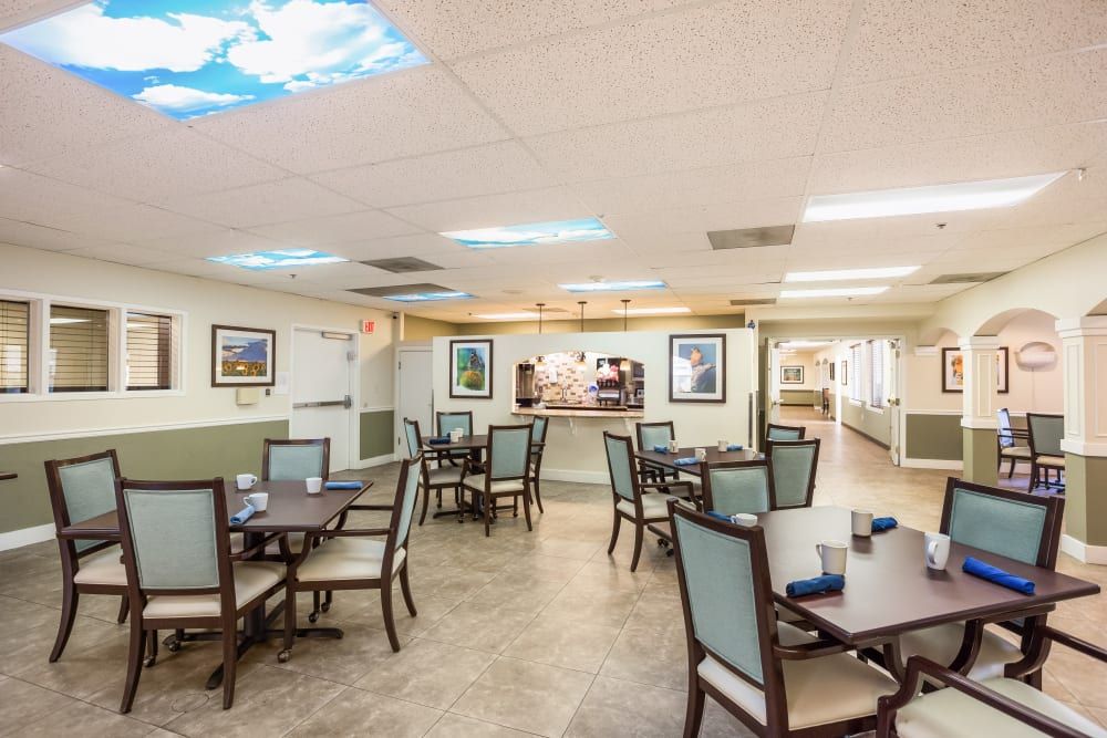 A spacious dining area with neatly arranged tables and chairs, featuring artwork on the walls and ceiling lights.