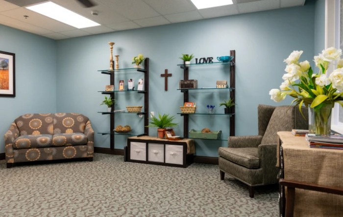 A cozy living room with blue walls, featuring comfortable chairs and decorated shelves.
