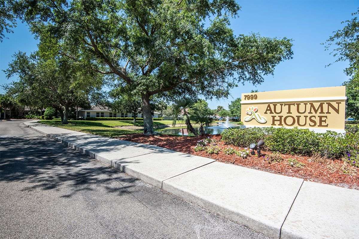 A landscaped entrance with a welcoming sign and walkway surrounded by trees.