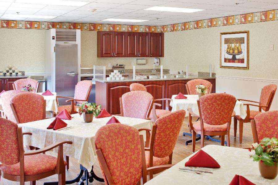 A cozy dining area with neatly arranged tables and chairs, featuring a small kitchen in the background.