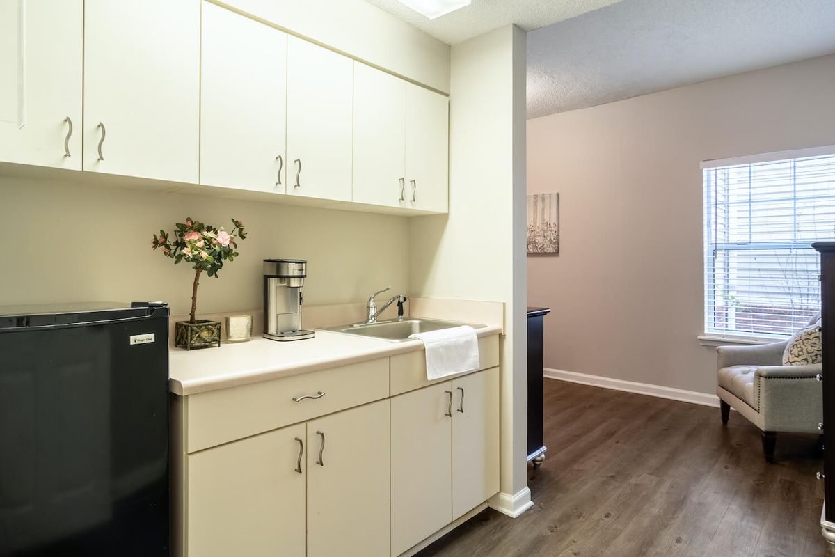 A modern kitchen area with white cabinets, a sink, and wood flooring.