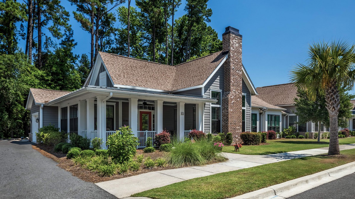A charming residential house with a porch, landscaped front yard, and prominent chimney.