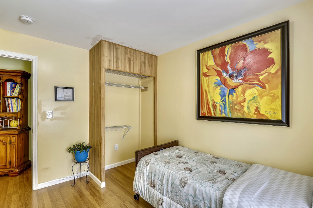A cozy bedroom with a single bed, colorful artwork on the wall, and a small plant near an open closet.