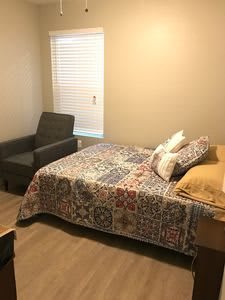 A cozy bedroom with a quilt-covered bed and an armchair near the window.