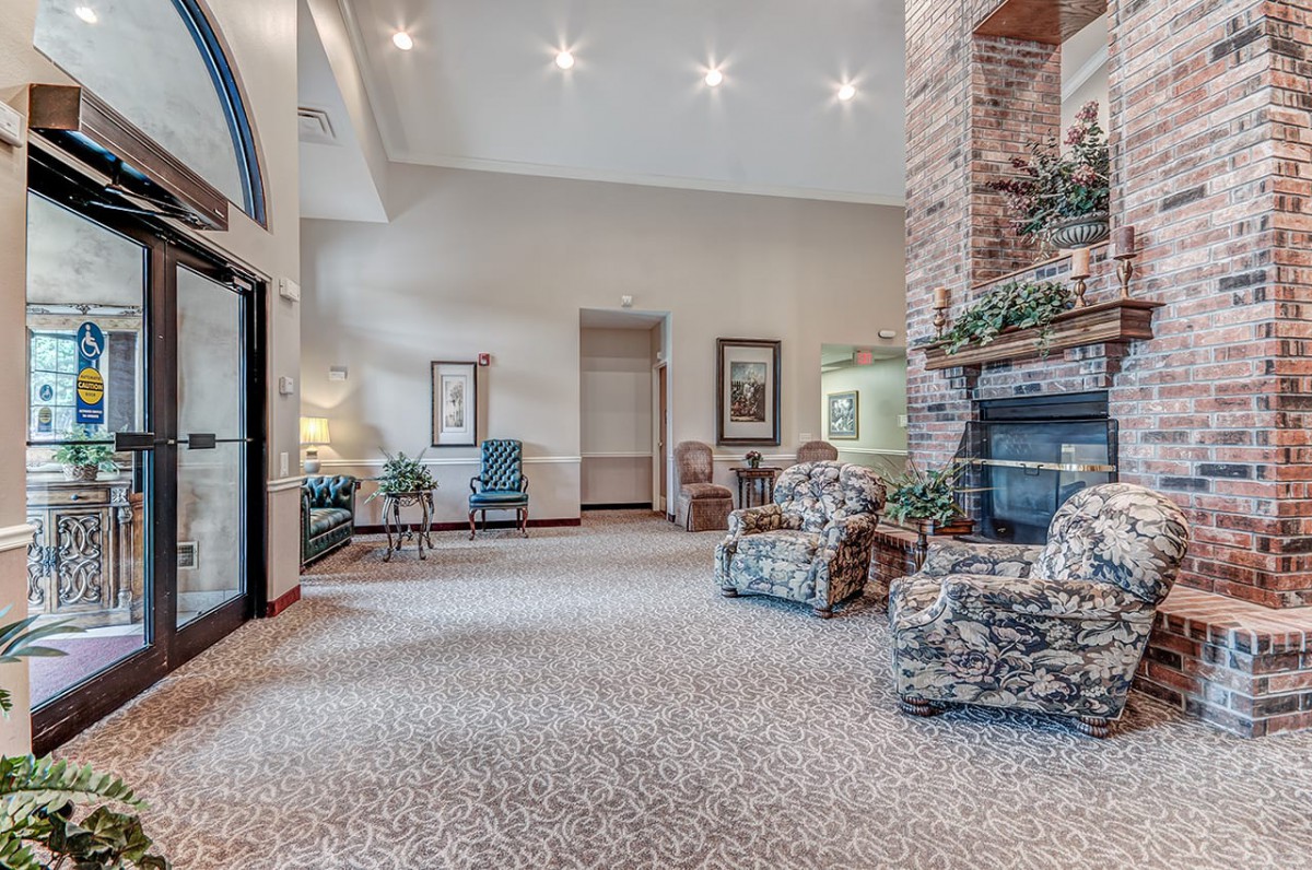 A spacious living room with a stone fireplace, comfortable armchairs, and decorative plants.
