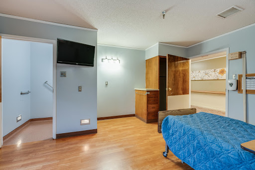 A modern bedroom with a wooden floor, featuring a television and minimalist furniture.