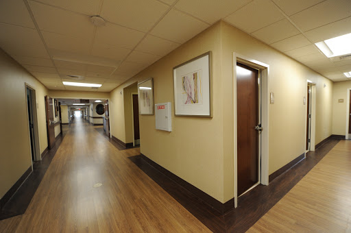 A view of a hospital corridor featuring a door and framed artwork on the wall.