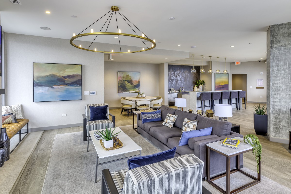 A modern living room with stylish furniture, artwork on the walls, and a large chandelier providing lighting.