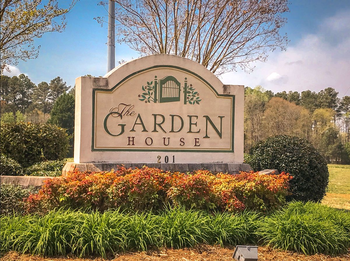 Entrance sign for The Garden House surrounded by landscaped greenery.