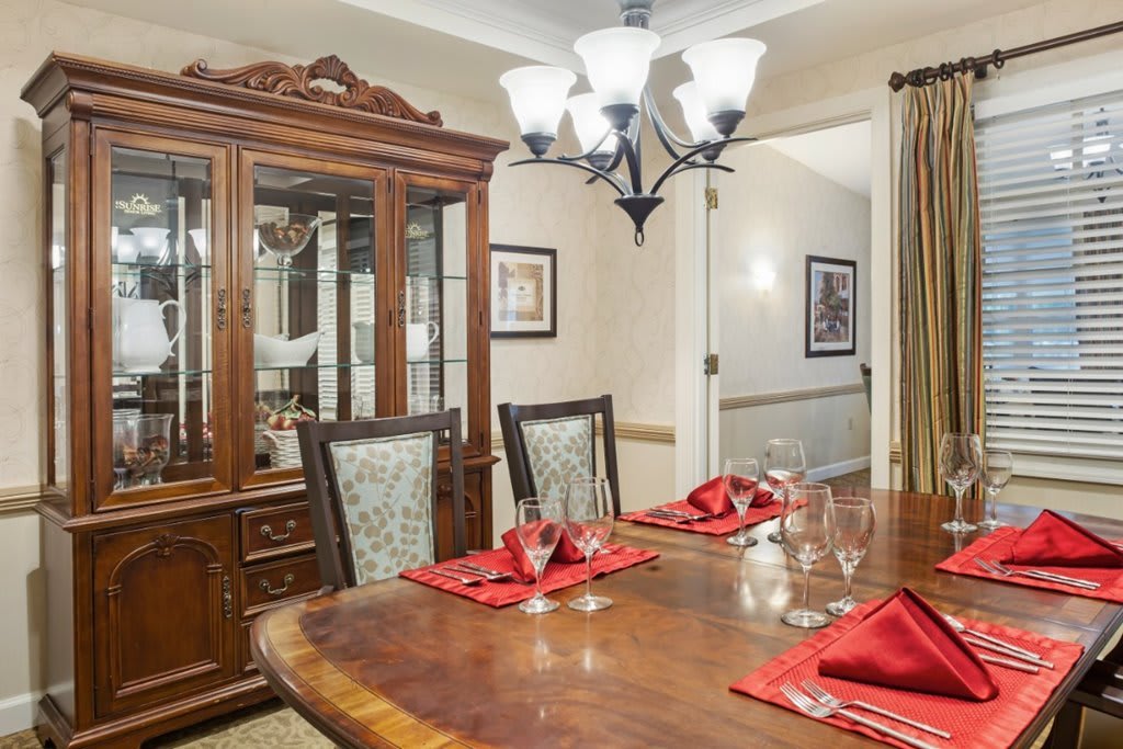 A well-appointed dining room with a wooden table set for dinner, featuring a chandelier and a china cabinet in the background.