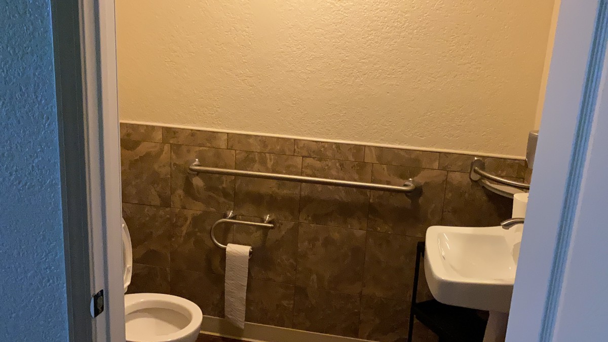 A bathroom with a toilet, a sink, and a handrail against a tiled wall.