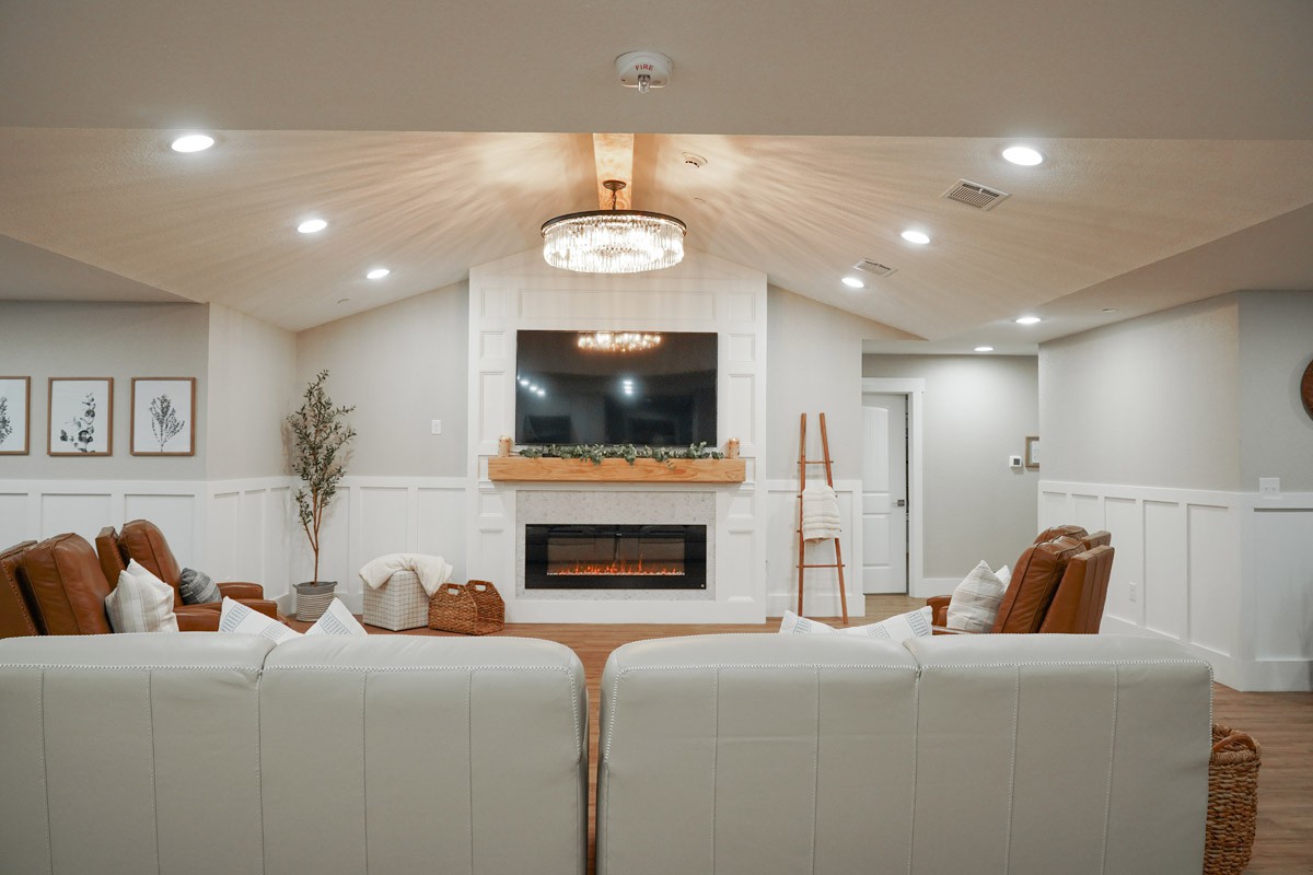 A modern living room featuring a fireplace, large TV, and elegant chandelier.