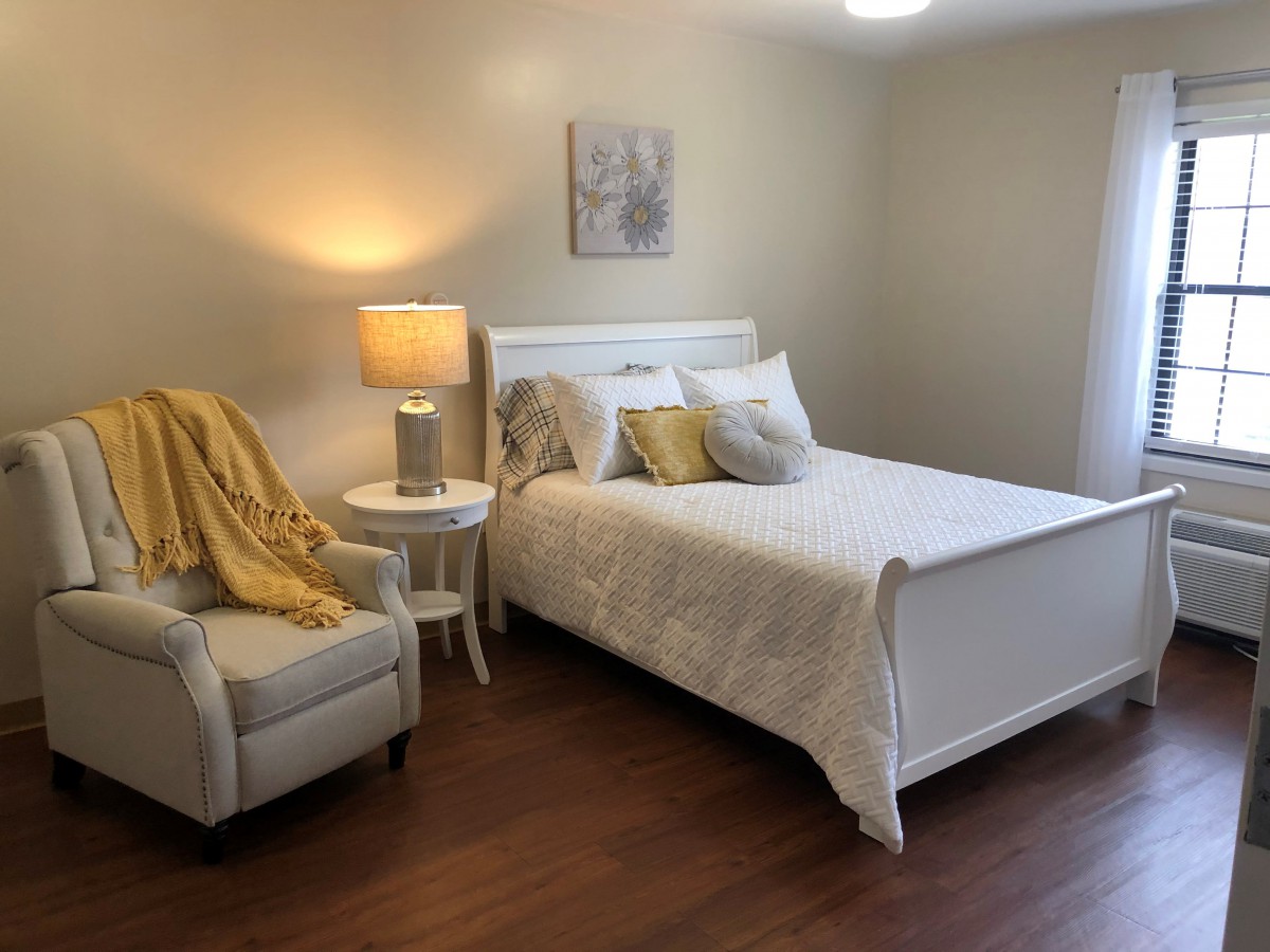 A cozy, well-lit bedroom with a bed, chair, and lamp.