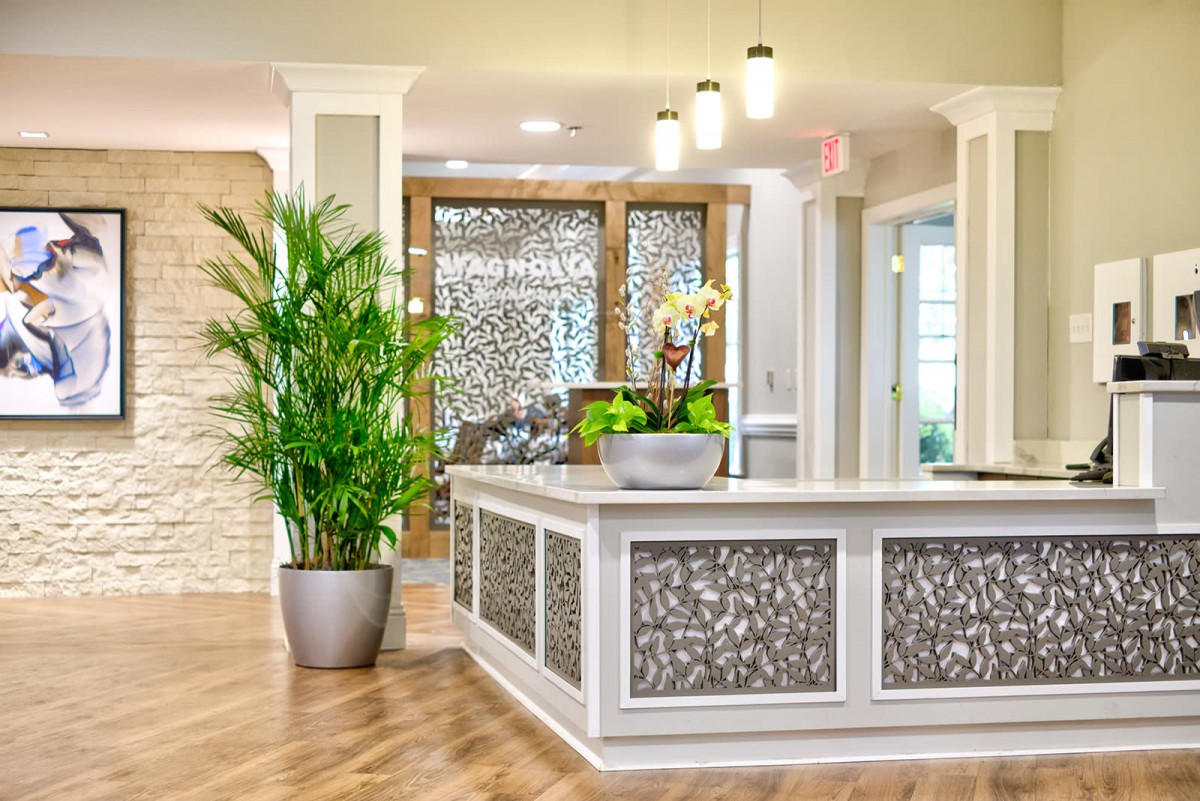 A modern reception area featuring a decorative desk with ornamental panels, potted plants, and elegant lighting.