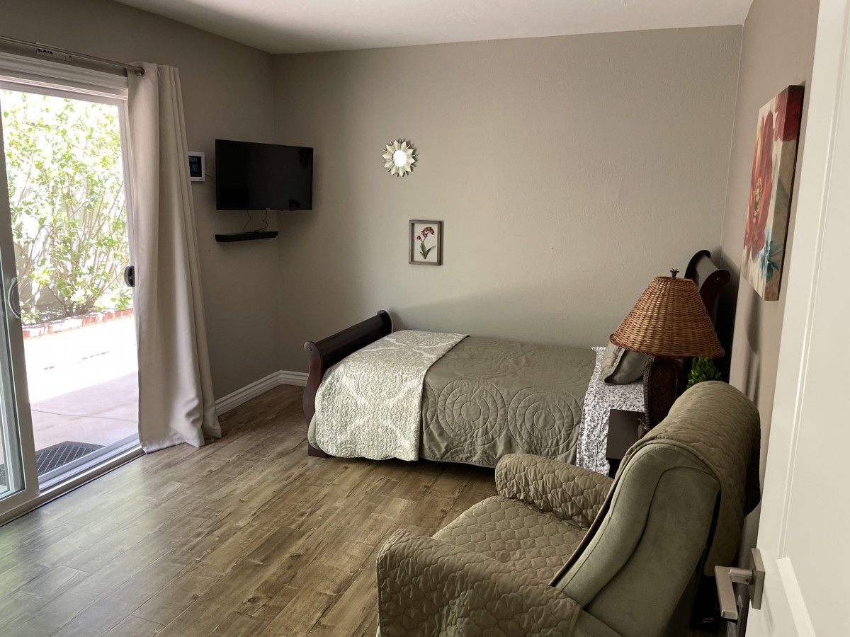A cozy bedroom with a small bed, armchair, and wall-mounted TV.