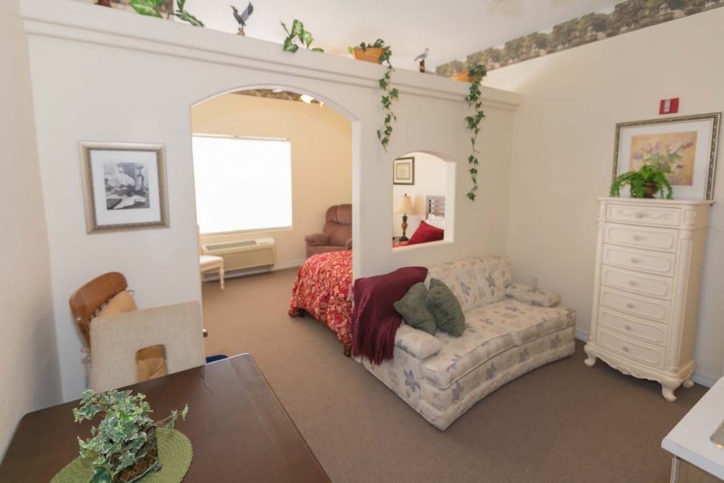 A cozy interior featuring a living area with a sofa, plants, and an adjoining bedroom.
