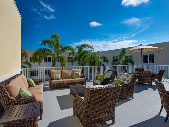 A sunny rooftop patio with comfortable wicker furniture and palm trees.