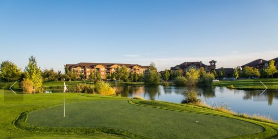 A peaceful golf course landscape with a lake and buildings in the background.