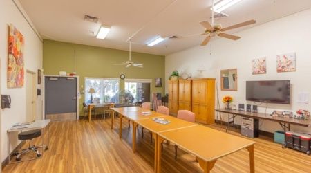 A spacious meeting room with a long table, chairs, and ceiling fans, featuring wooden floors and decorative elements.