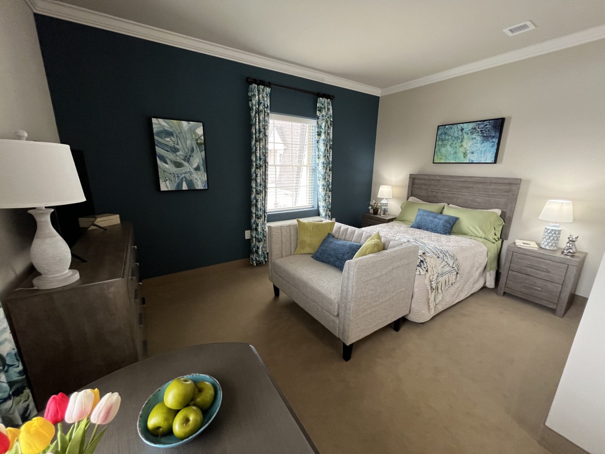 A cozy bedroom interior featuring a bed with decorative pillows, a small sofa, and modern artwork on the walls.