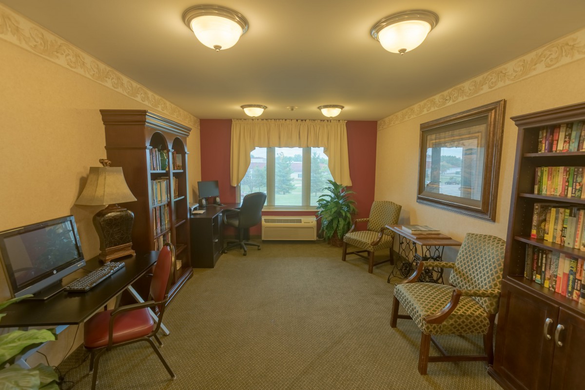 A cozy living room with multiple chairs, bookshelves, and a large window letting in natural light.