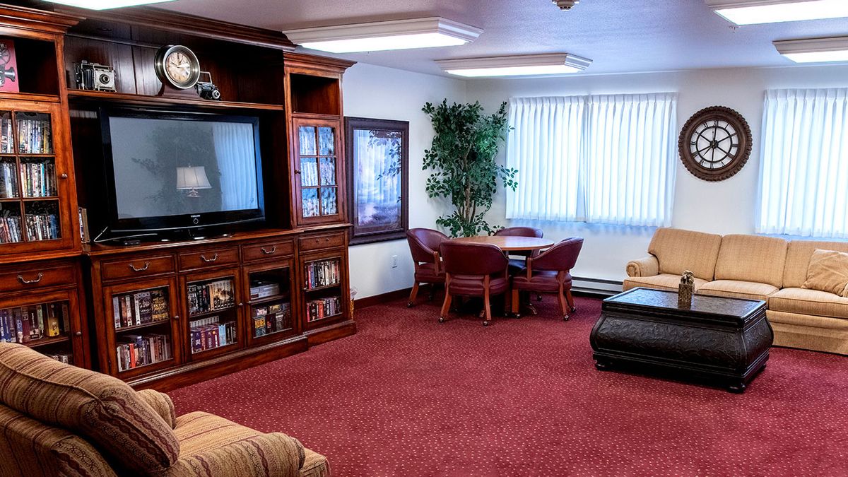 A cozy living room with a large TV, comfortable seating, and a red carpet.