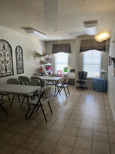 A spacious multi-purpose room with tables and chairs set up for a gathering, featuring natural light from the windows.