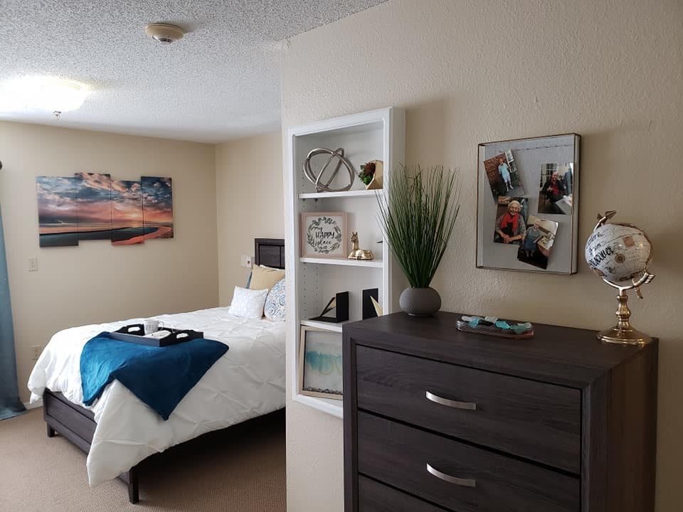 A well-decorated bedroom featuring a bed, dresser, and wall-mounted shelves with artwork.